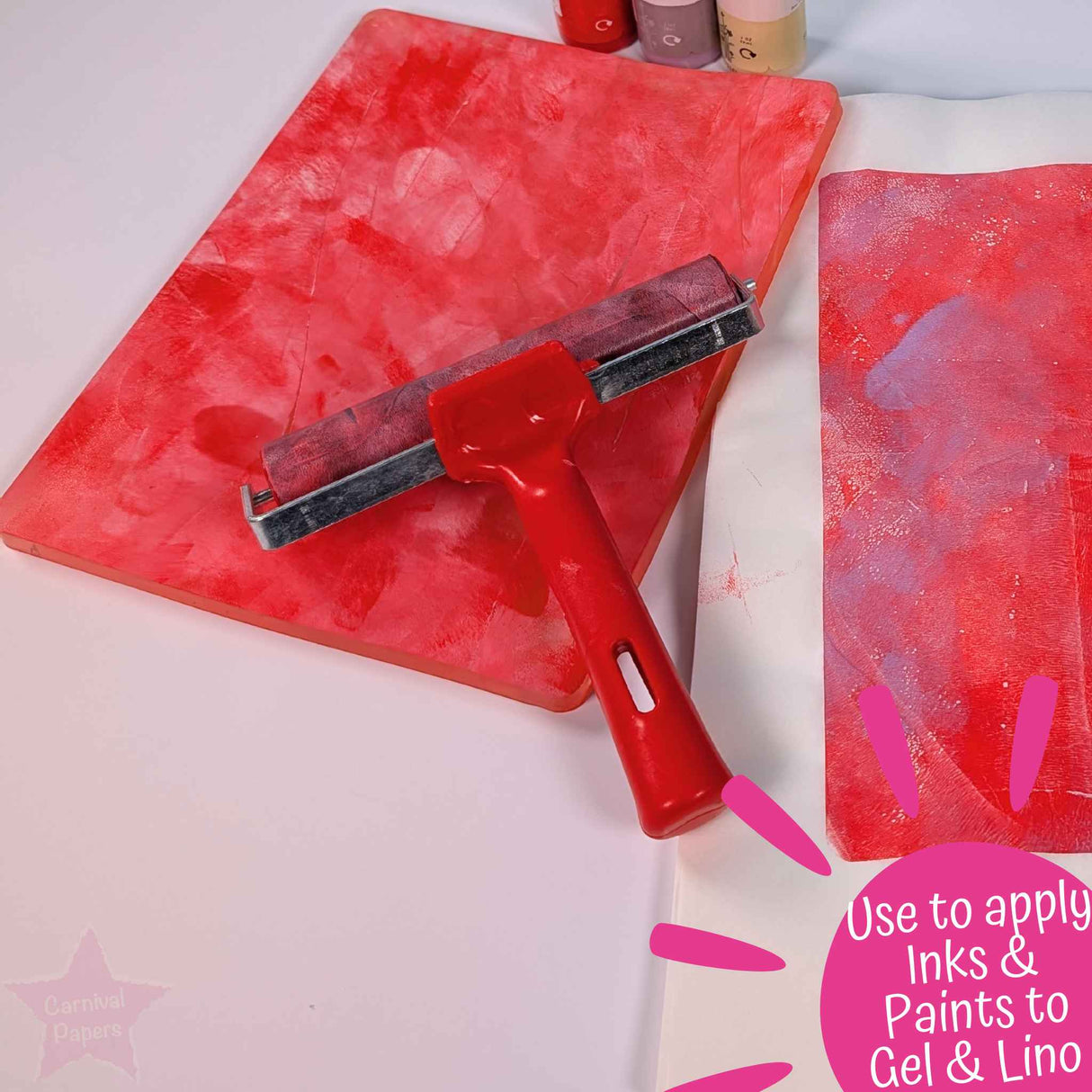 Red brayer roller being used with wet strength tissue paper with pink paint strokes, used to apply inks and paints to gel plate and lino sheets