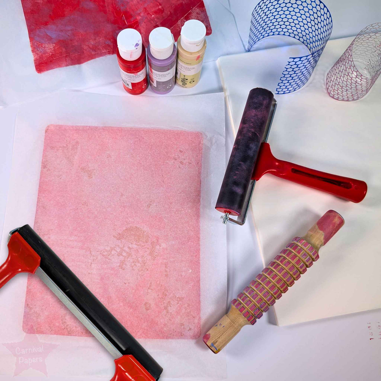 Art supplies including a brayer roller, tissue paper and ink bottles on a white surface.