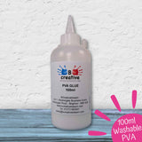 A 100ml bottle of B Creative PVA Glue, 99% washable, shown on a rustic blue wooden surface against a white textured wall. A pink circular badge in the bottom right corner reads '100ml Washable PVA'.